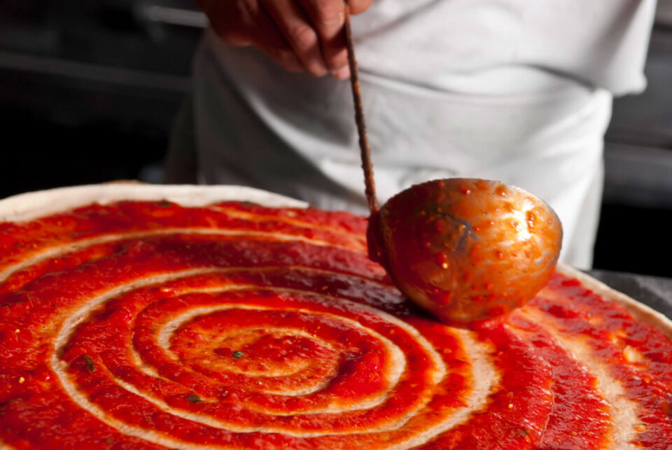 man adding red sauce to pizza crust